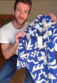 Korte mouw shirt in blauw met witte abstracte bladeren en geometrische patronen; labels zichtbaar, met merk- en streepjescodes.