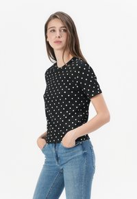 Black t-shirt with white polka dots, short sleeves, round neckline, and a fitted design, paired with light blue jeans.