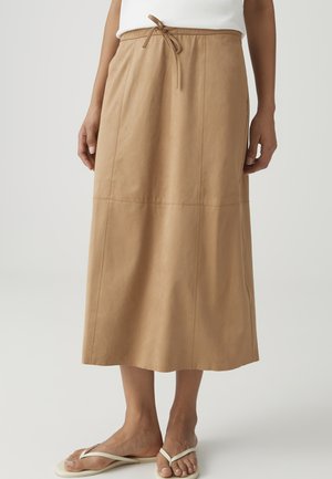 Beiger Midirock mit Kordelzugbund, kombiniert mit weißen Flip-Flops und einem weißen Oberteil, gezeigt vom mittleren Oberkörper bis zu den Füßen.