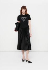 Black Guess t-shirt with crystal logo, pleated black midi skirt, black handbag, and black high-heeled shoes. Simple and monochromatic design.