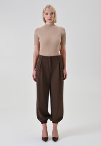 Top beige a maniche corte a coste abbinato a pantaloni marroni a vita alta con righe sottili, polsini elasticizzati e tacchi neri appuntiti.