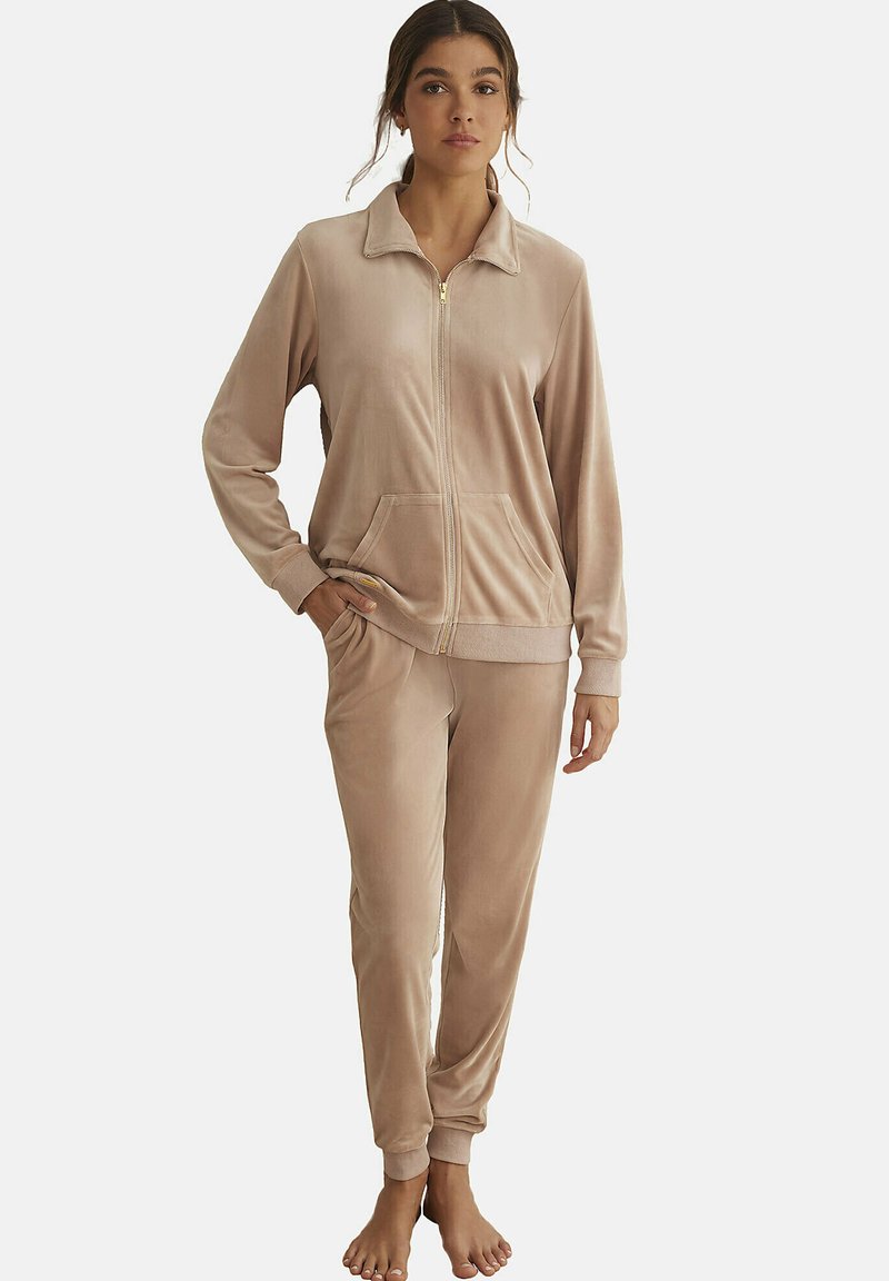 Ensemble de survêtement en velours de couleur beige doux, comprenant une veste zippée avec un col et des poches, associée à un pantalon ajusté assorti.