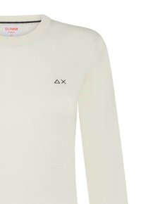 Maglione lavorato a maglia di colore crema con colletto rotondo e maniche lunghe, caratterizzato da un piccolo logo nero sull'area sinistra del petto. Texture morbida.