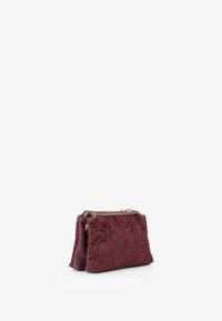 Borsetta in tessuto bordeaux con ricami floreali intricati, chiusura con zip e parte superiore arrotondata. Superficie texture con una sensazione morbida e vellutata.