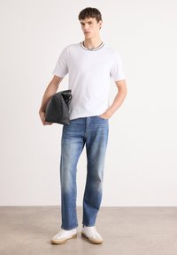 Hvid kortærmet t-shirt med en sort kantkrave, lyseblå jeans og hvide sneakers med beige såler; bærer en sort taske.