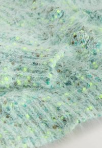 Texturiertes, hellblaues Strickgewebe mit flauschigen Fasern und Sprenkeln von Gelb und Braun; zeigt ein lockeres, luftiges Webmuster.