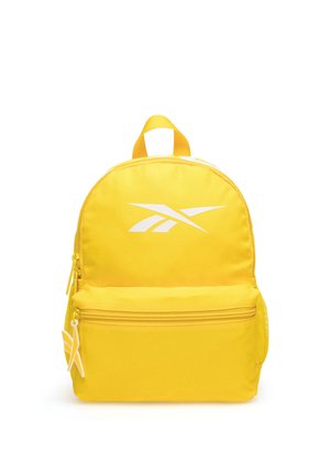 Mochila amarilla con bolsillo frontal con cremallera, logotipo blanco en la parte delantera, asa superior y bolsillo lateral de malla, fotografiada sobre fondo blanco.