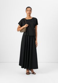 Ensemble noir deux pièces composé d'un haut à manches courtes et d'une longue jupe fluide. Tissu lisse, design minimaliste, avec un sac à main assorti.