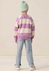 Sweatshirt rayé violet et crème avec des poignets côtelés, étiquette à l'arrière, associé à un jean bleu clair retroussé et des chaussures beiges.