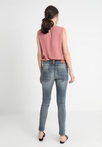 Top rosa sin mangas con detalle de ojal en la espalda, combinado con unos jeans ajustados azul con un acabado desgastado y dos bolsillos traseros.