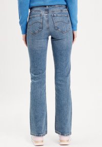 Blue flared jeans with a high waist, featuring back pockets and subtle stitching details. The fabric has a slightly faded appearance.