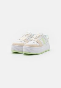 Sneakers platform bianchi e beige con suola verde. Le caratteristiche includono una tomaia in pelle liscia, dettagli in suede e perforazioni sulla punta.