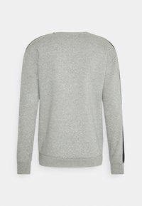 Sudadera de manga larga gris claro con rayas negras a lo largo de las mangas, puños acanalados y dobladillo acanalado, vista desde la parte de atrás.