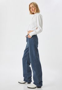 Camisa corta blanca combinada con pantalones de pierna ancha a rayas azules y botas de tobillo blancas. Tejido suave, camisa ajustada, ajuste relajado en los pantalones.