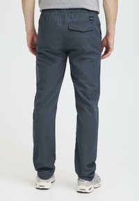 Men's gray elastic-waist pants with a textured pattern, a back pocket, and tapered legs, paired with light gray athletic shoes.