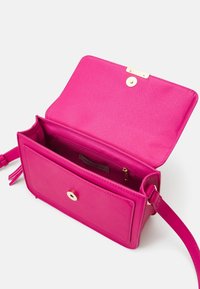 Fuchsiová kožená taška přes rameno s klopou, zlatými kovovými detaily a podšívkou, která obsahuje zipovou kapsu a značkový štítek.