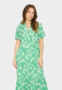 Rochie maxi verde cu imprimeu floral, cu mâneci scurte, decolteu în v, design în straturi și modele florale albe pe întreaga suprafață. Material ușor, cu o textură moale.