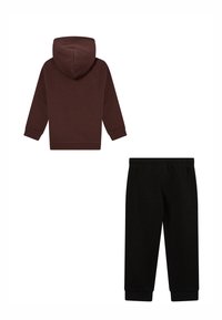 Sudadera con capucha marrón de acabado texturizado y pantalones de chándal negros con pierna ajustada y cintura elástica. Ambos están hechos de una tela suave.