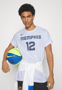 T-shirt en coton blanc avec "MEMPHIS" et "12" en lettres bleues marine, accompagné d'un ballon de basket multicolore et d'un sweat-shirt blanc noué autour de la taille.