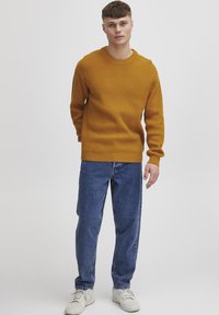 Mustard ribbed sweater with a round neck, paired with loose blue denim jeans and white sneakers, featuring a relaxed fit and textured fabric.