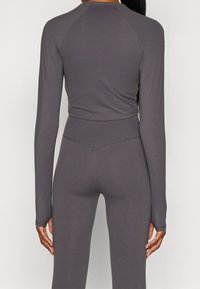 Šedý dlouhý rukáv zkrácený top z elastického materiálu, s hladkým povrchem a minimálními švy, spárovaný s odpovídajícími legínami s vysokým pasem.
