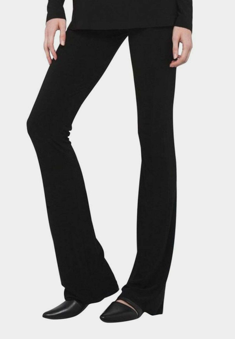 Pantalons évasés noirs en tissu extensible, présentant une texture lisse et une silhouette de jambe allongée. Associés à des chaussures pointues noires.