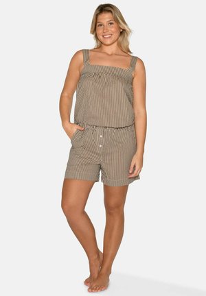 Młoda kobieta uśmiecha się, stoi boso, ubrana w bezrękawnik i pasujące szorty w pionowe, beżowo-białe paski z kieszeniami.