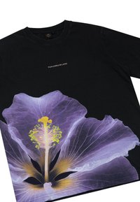 Zwart katoenen t-shirt met een grote paarse bloemenafbeelding op de voorkant, met gele en groene accenten, en "TOMORROWLAND" gedrukt erboven.