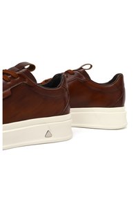 Sneaker in pelle marrone con suole in gomma bianche, caratterizzati da dettagli testurizzati, lacci tondi e un logo triangolare sul lato.