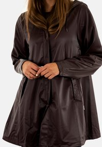 Waterdichte, bruin hoodiejas met een losse pasvorm. Beschikt over twee voorzakken en een ritssluiting aan de voorkant. Gladde, glanzende textuur.