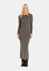 Vestido largo gris de canalé con mangas largas, adornado con pequeñas cuentas. Silueta ajustada; combinado con botas negras hasta el tobillo.
