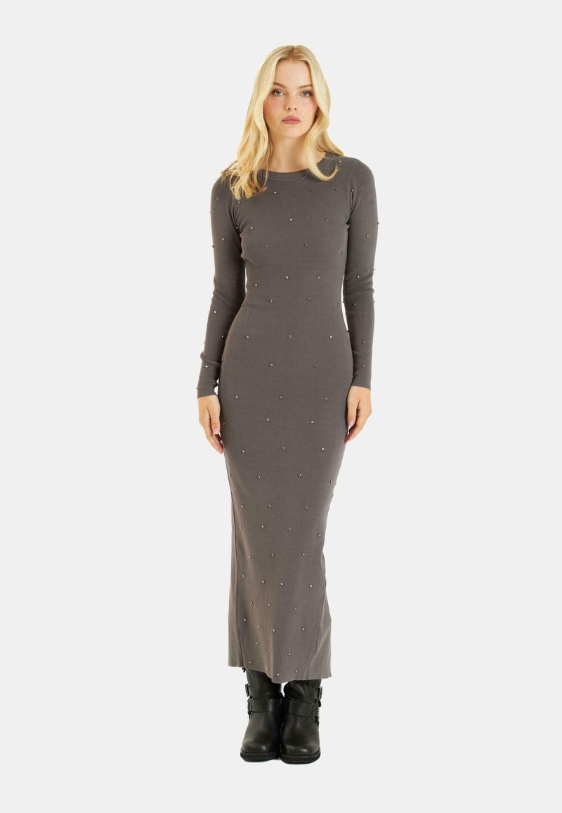 Vestido largo gris de canalé con mangas largas, adornado con pequeñas cuentas. Silueta ajustada; combinado con botas negras hasta el tobillo.