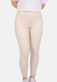 Beige Leggings mit hoher Taille aus dehnbarem Stoff, mit glatter Oberfläche und figurbetontem Schnitt, kombiniert mit weißen Sneakers.