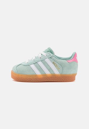 Sneaker in suede verde menta con tre strisce bianche, accento rosa sul tallone e suola in gomma. Presenta lacci bianchi e una parte superiore testurizzata.