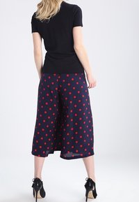 Culotes azul marino con lunares rojos y un diseño fluido, combinados con una blusa ajustada de manga corta negra y zapatos de tacón alto negros.