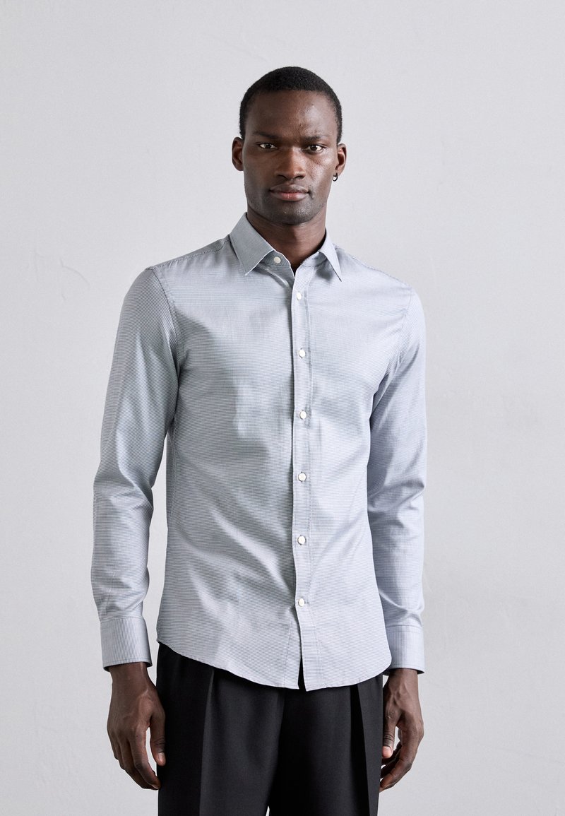 Light blue button-up shirt with subtle stripes, long sleeves, standard collar, and white buttons; paired with black pants.