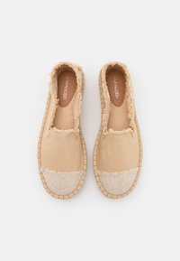 Beige espadriller med frynsete kanter, overdel i lerret og en kontrasterende teksturert tå. Snudd jute såle, rund form, uformelt design.