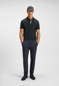 Sort polo shirt med en kontraststribe på kraven, parret med marineblå bukser og sorte sneakers. Tilbehøret inkluderer en matchende kasket.