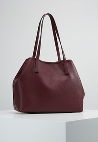 Bordeauxrode leren totebag met een gestructureerd oppervlak, brede opening, dubbele schouderbanden en een gestructureerde vorm. Geen zichtbare metalen onderdelen of accenten.