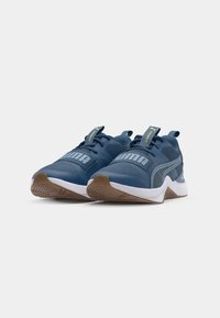Blå atletiska sneakers med texturerade mesh-material, vita och gummisulor, samt framträdande varumärkeslogotyp. Har en looper på hälen och snörningsdesign.