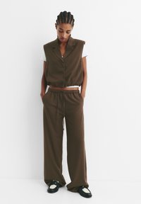 Top senza maniche marrone a costine con colletto, abbinato a pantaloni a gamba larga coordinati e scarpe nere con un accento bianco.