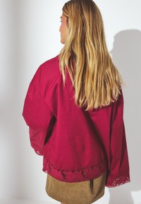 Cranberryfarbene, übergroße Bluse aus leichtem Stoff, mit Spitzenbesatz am Saum und weiten Ärmeln, die eine lockere Silhouette schaffen.