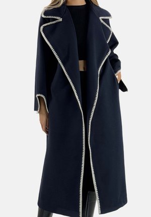 Abrigo azul marino con acabado texturizado, con ribete blanco en forma de ondas a lo largo de los bordes y un cuello ancho. Ajuste holgado con mangas largas.