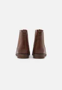 Bottines en cuir marron avec des panneaux élastiques sur les côtés, des talons en bois empilés et une texture lisse. Le design est dans le style classique Chelsea.