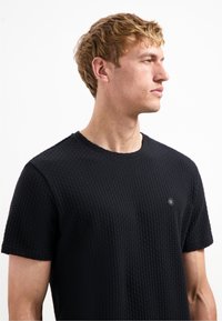 Zwarte textuur T-shirt met korte mouwen, voorzien van een ronde halslijn en een klein hexagonaal logo op de borst.
