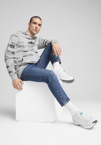 Gray sweatshirt with black graphic designs, blue denim jeans with frayed hem, and white sneakers with teal accent and textured sole.