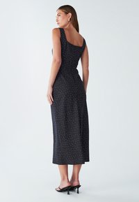 Crna midi haljina s bijelim točkicama, kvadratnim izrezom i širokim naramenicama. Tkanina je glatka, s uskim strukom i lepršavom suknjom.