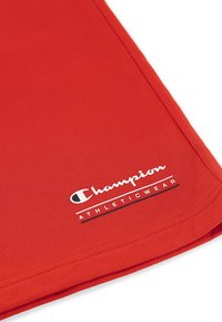 Czerwony materiał sportowy z teksturowanym ryflem; posiada białe logo "Champion" oraz czarny napis "ATHLETIC WEAR" poniżej. Czyste krawędzie i szwy.