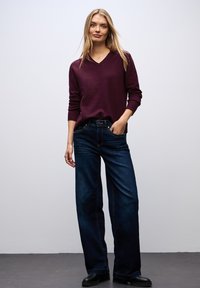 Burgundy v-ringad stickad tröja som matchas med vida mörka denimjeans. Slät textur, avslappnad passform, med en lätt glans på jeansen.