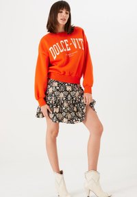 Rode sweatshirt met witte tekst en een geribbelde zoom, gecombineerd met een zwarte bloemenrok met ruches. Witte enkelbootjes met studs.